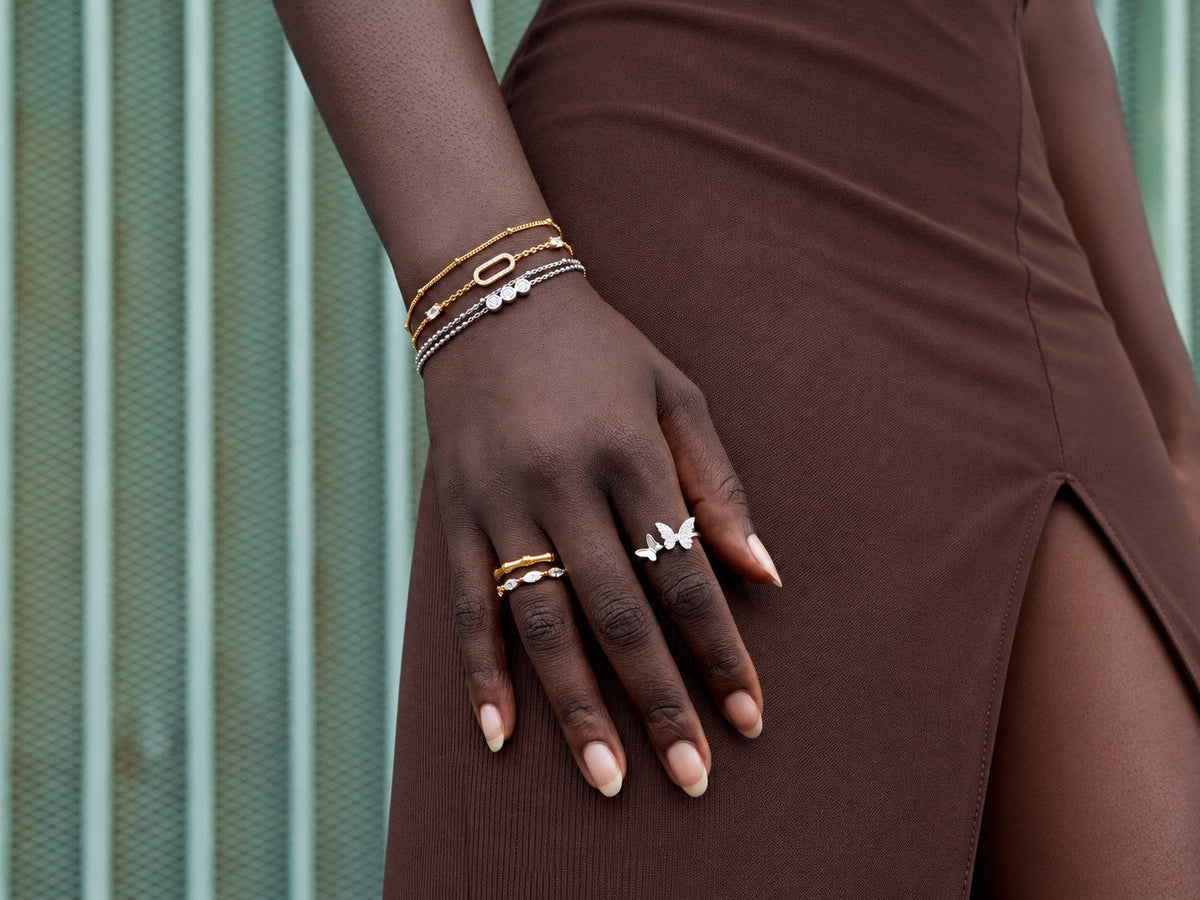 Mano con pulseras y anillos de acabados dorados y plateados sobre vestido marrón